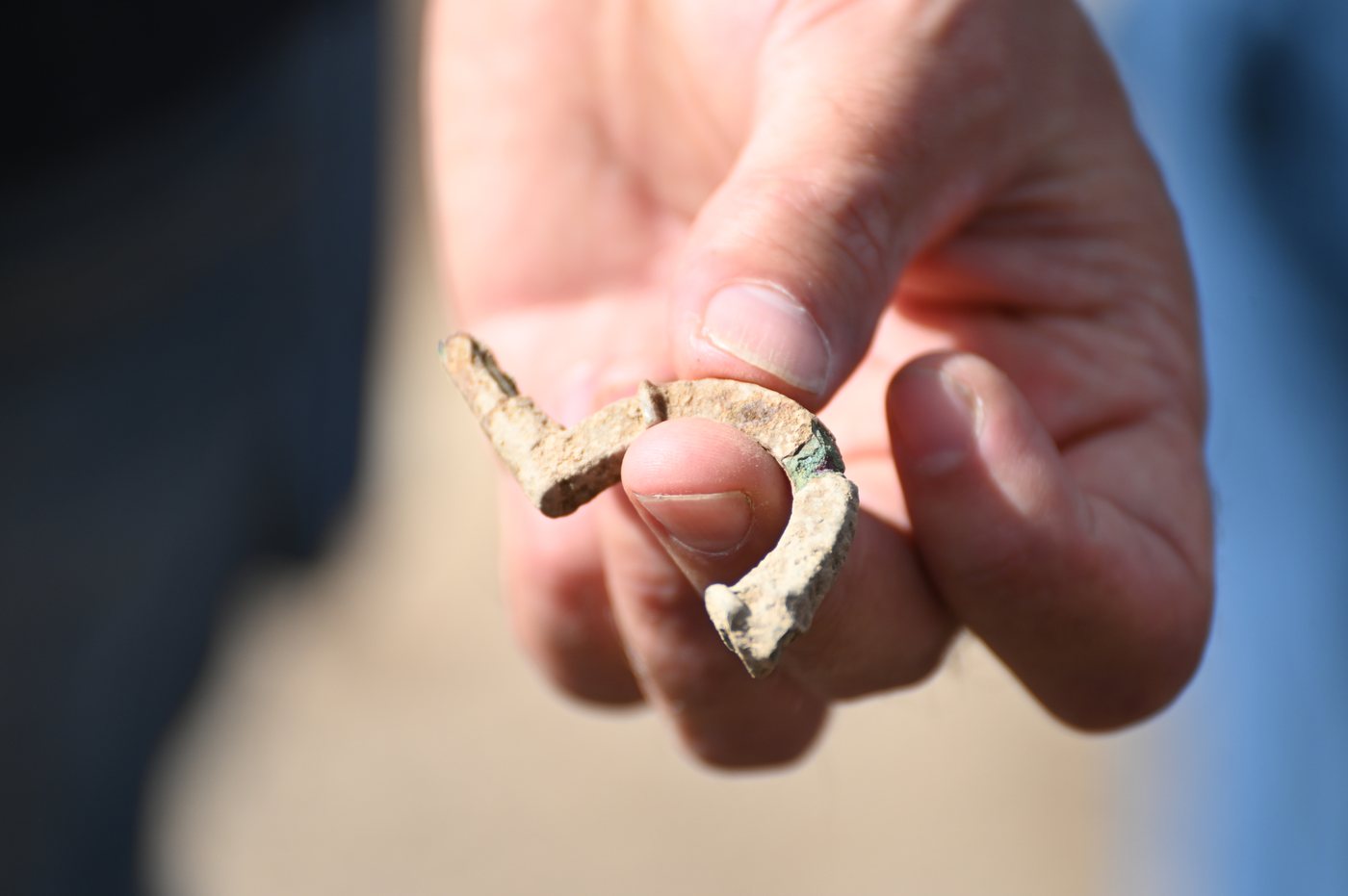 Kapersburg tapınağının yanında bulunan geç antik döneme ait küçük metal fibula, bir arkeoloğun parmakları arasında