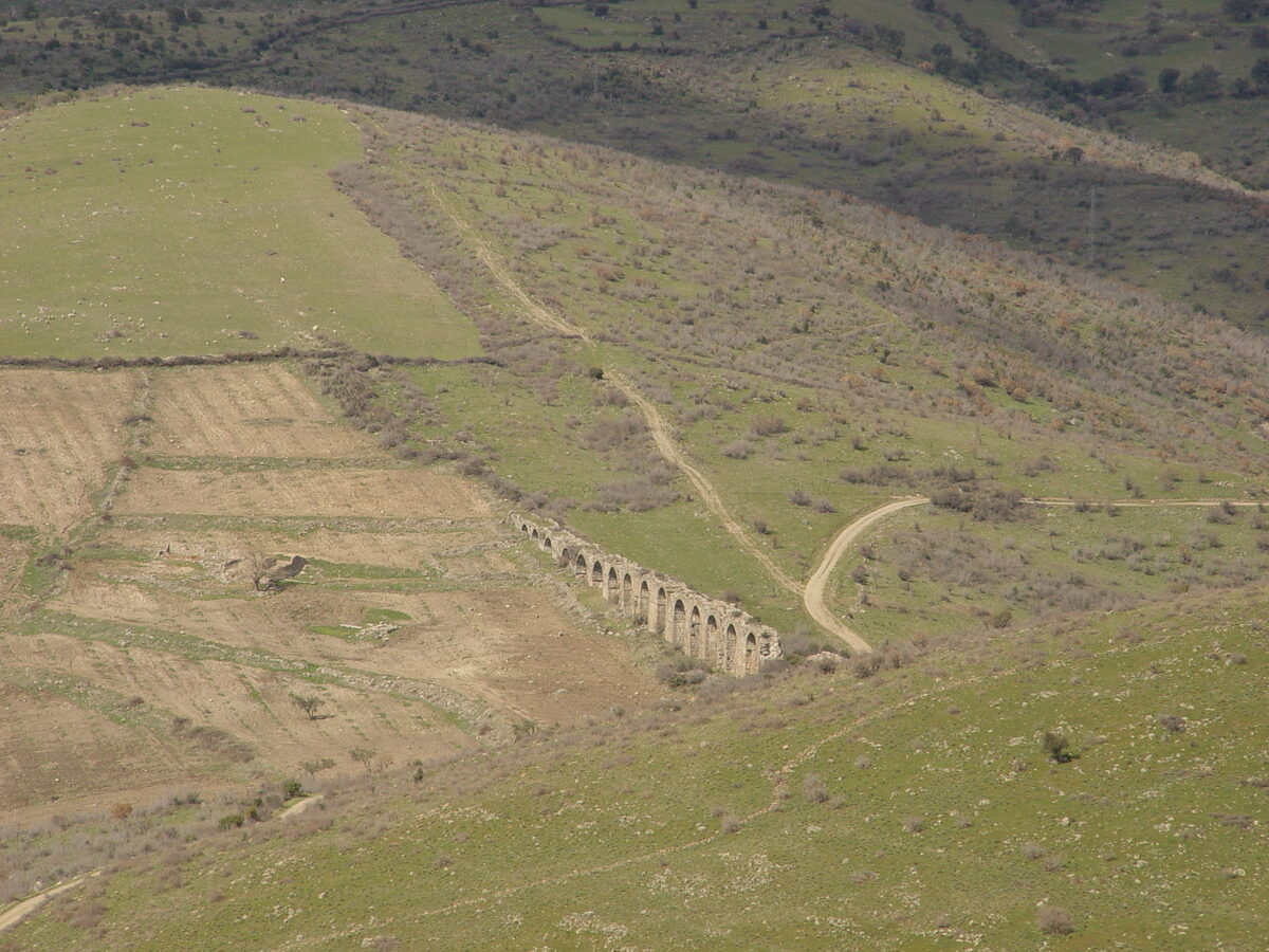 Bergama akropolünden kuzeye bakış: yeşil yamaçlar arasında bir vadi, vadinin ortasında taştan bir kemer dizisi ve kıvrılan toprak yollar