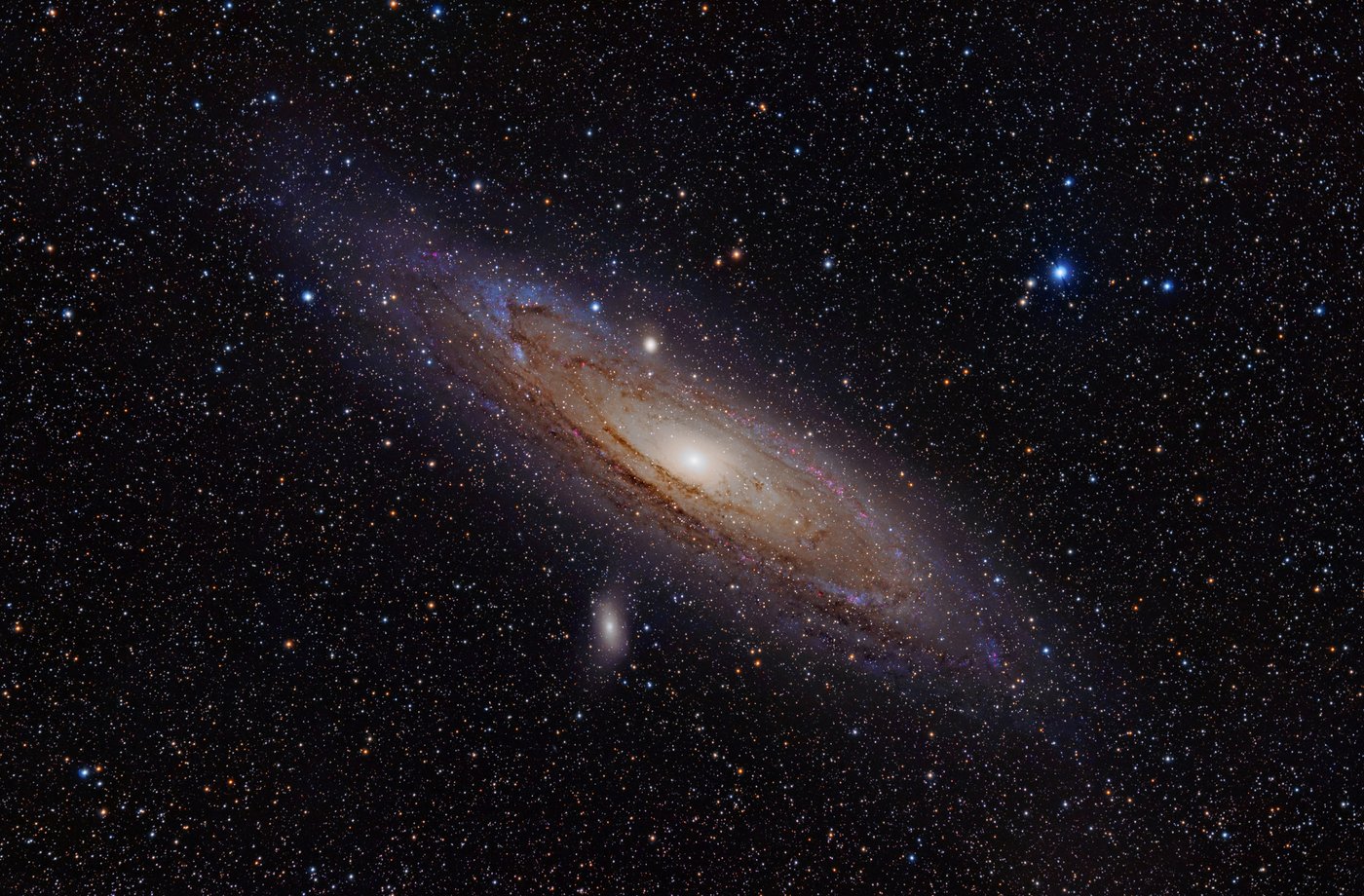 Andromeda galaksisi: yamuk duran parlak çekirdekli sarmal disk, toz şeritleri ve iki küçük uydu galaksi