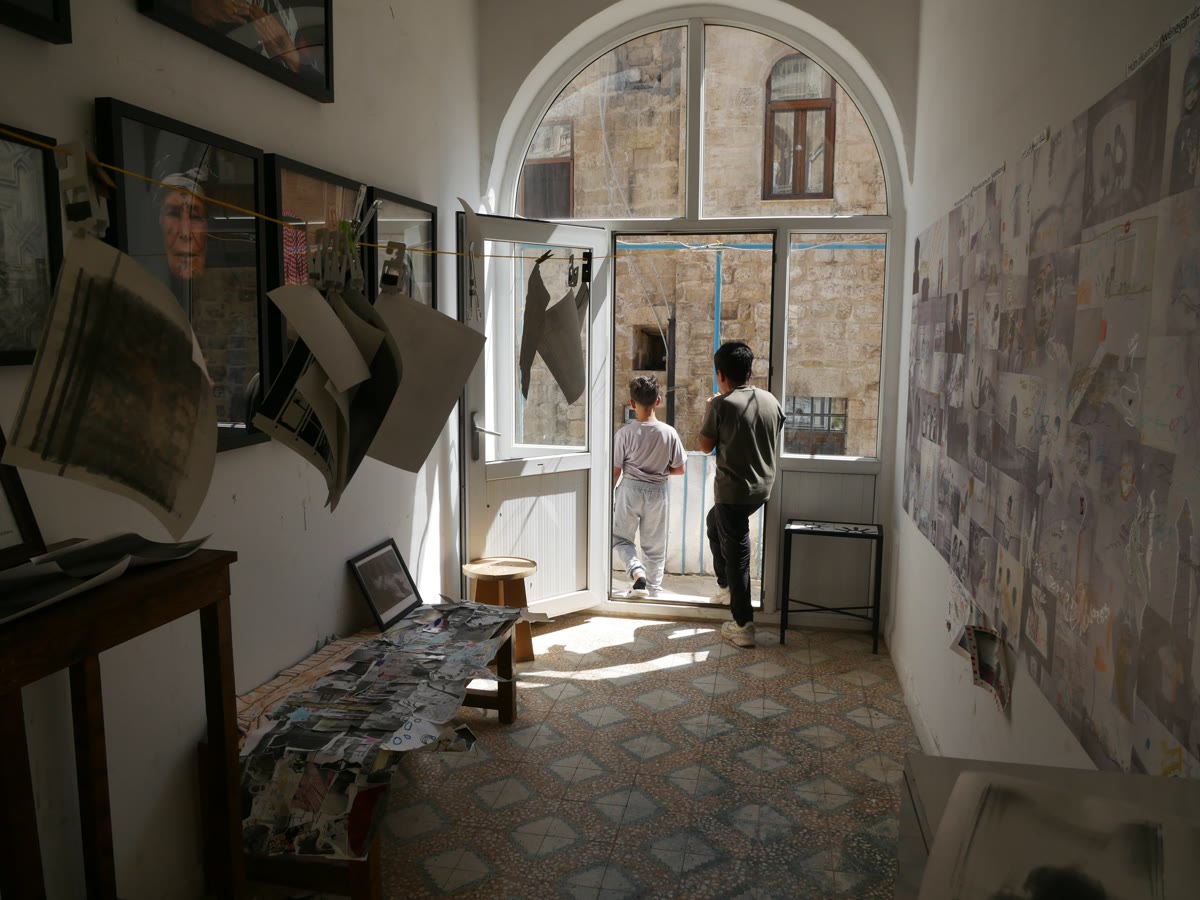 Mardin'deki Fotohane atölyesinde iplere asılı siyah beyaz baskılar, duvarda çocuk çizimleri ve kemerli kapıdan avluya çıkan iki çocuk