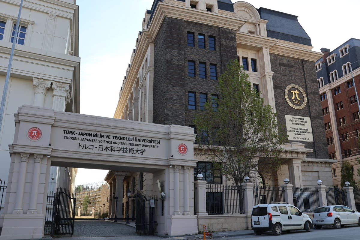 Ankara'daki Türk-Japon Bilim ve Teknoloji Üniversitesi'nin taş kemerli giriş kapısı ve üzerinde Türkçe, İngilizce ve Japonca yazan okul adı, arkada TJU amblemli bina