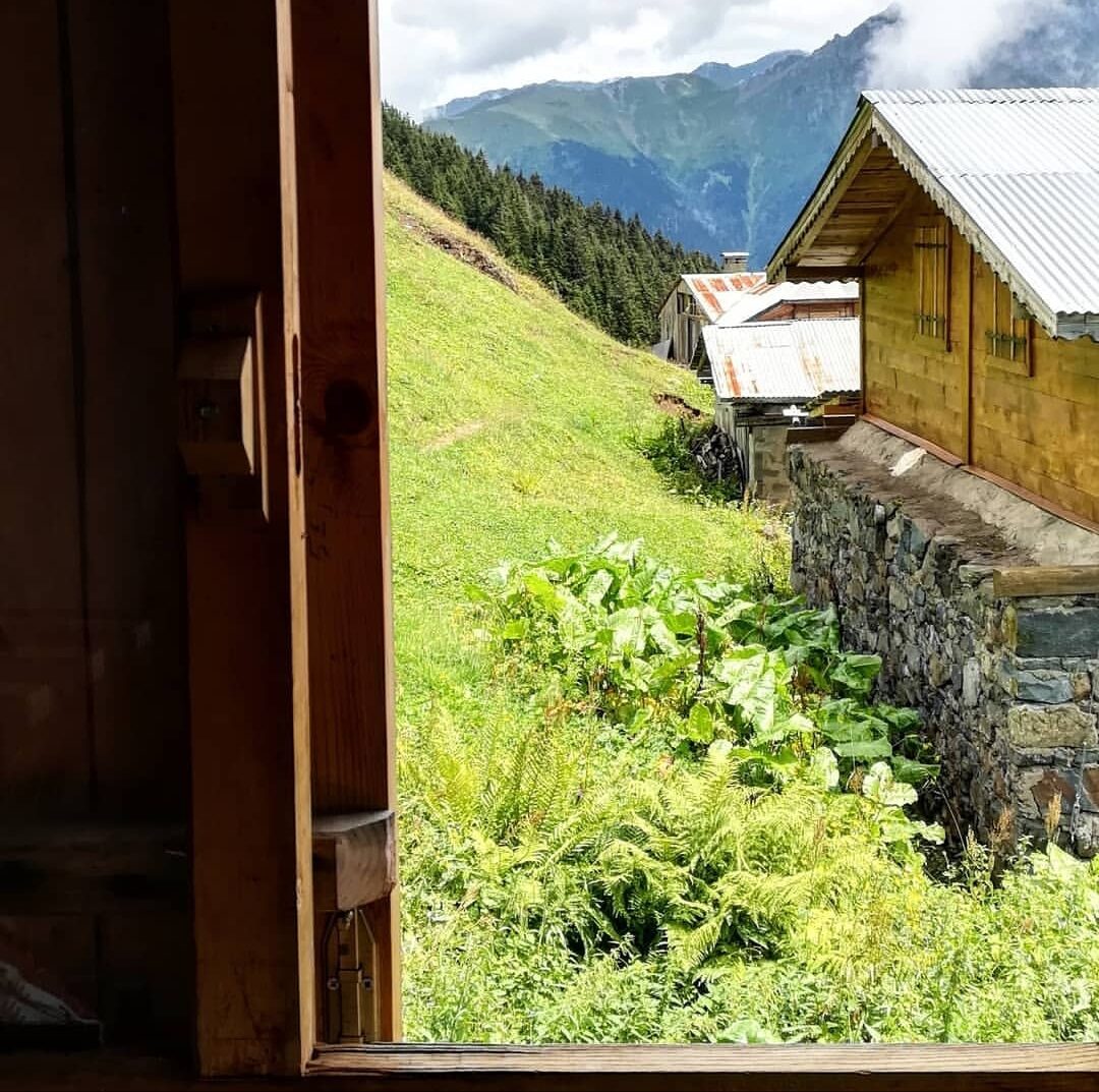 Ahşap yayla evinin penceresinden çayır ve dağ manzarası