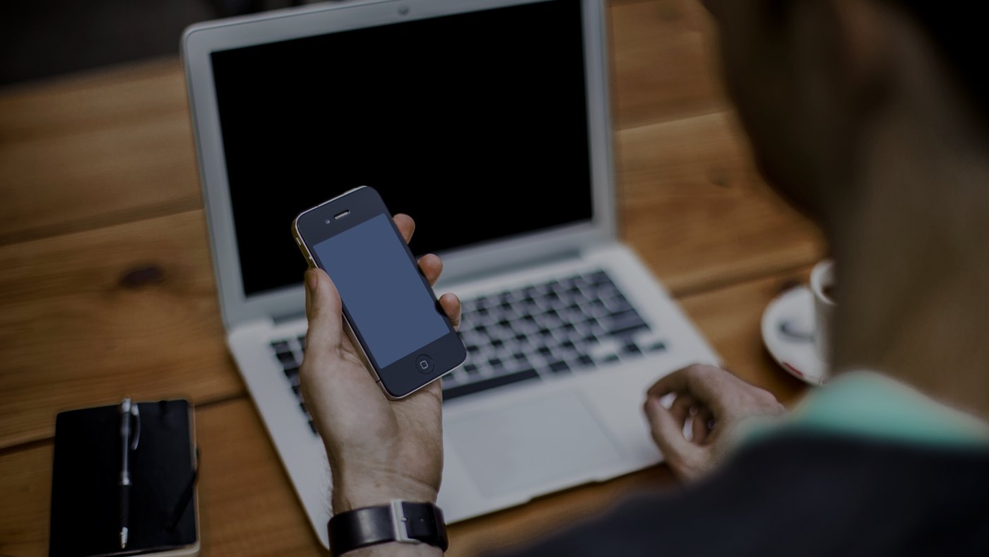 Masada dizüstü bilgisayar, elinde telefon olan bir kişi
