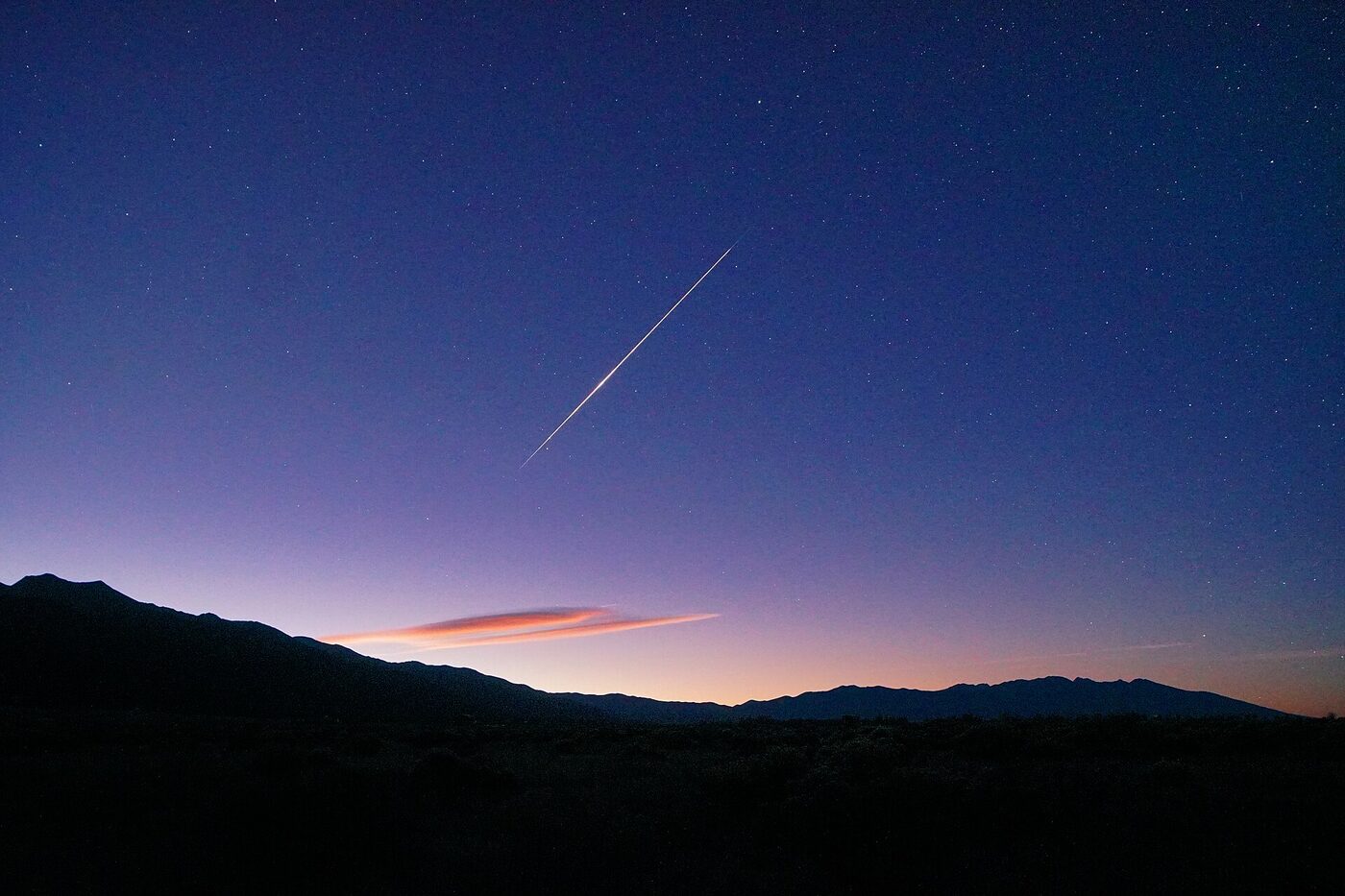 Şafak öncesi lacivert gökyüzünde tek bir meteor izi, ufukta dağ silueti