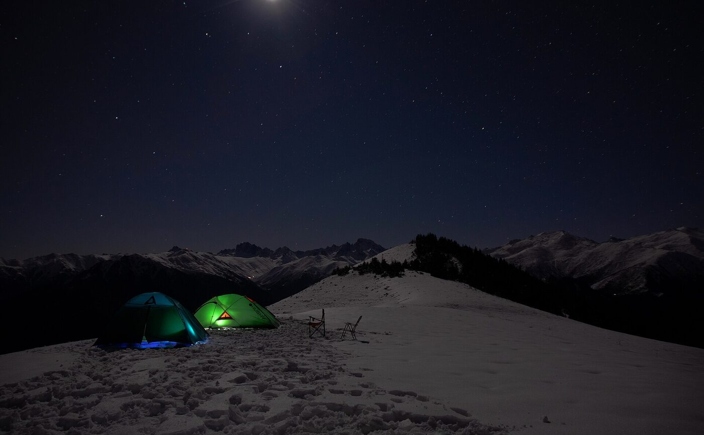 Karlı Pokut sırtında gece ışık saçan iki çadır ve yıldızlı gökyüzü