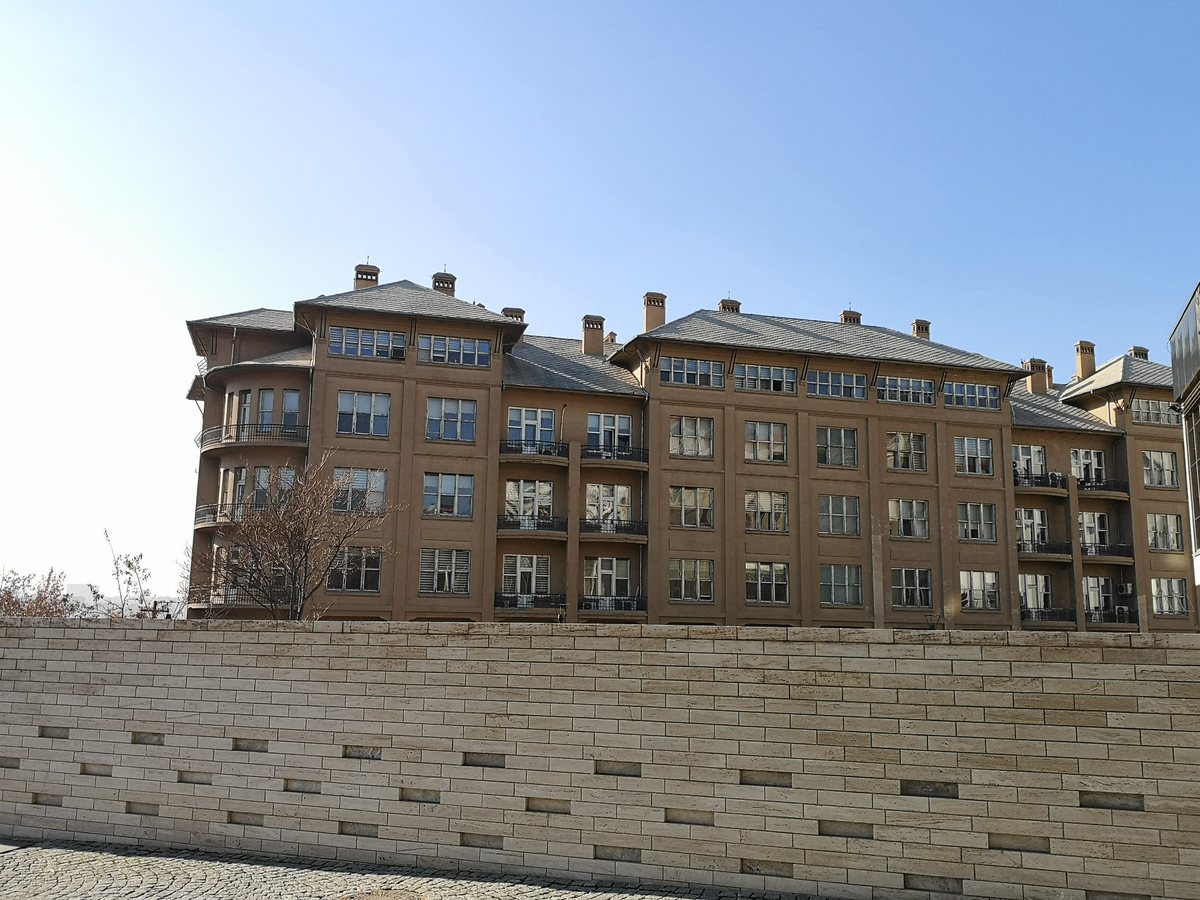 Açık mavi gökyüzü altında kahverengi cepheli, kiremit çatılı ve bacalı beş katlı II. Evkaf Apartmanı; önde taş bir duvar
