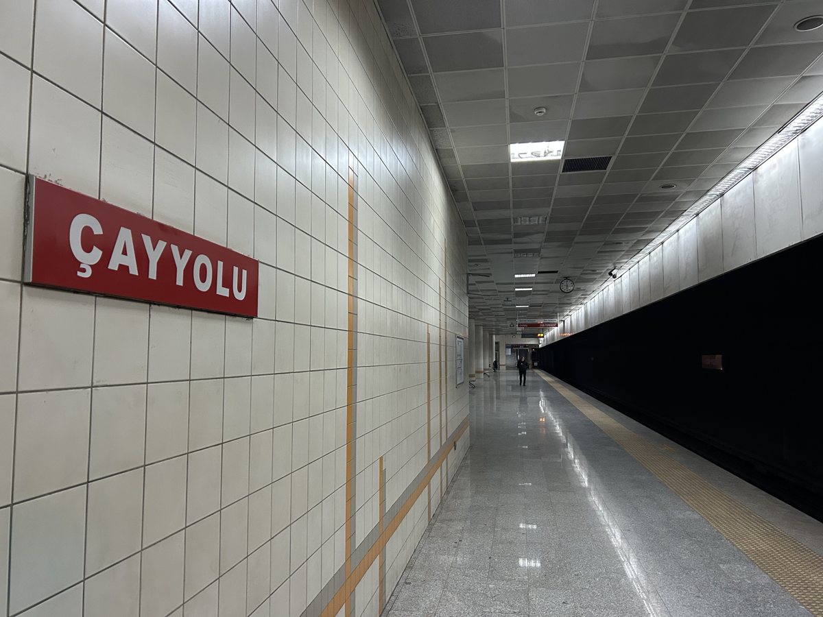 Çayyolu metro istasyonunun beyaz fayanslı peronu, duvarda kırmızı zemin üzerine beyaz harflerle ÇAYYOLU levhası