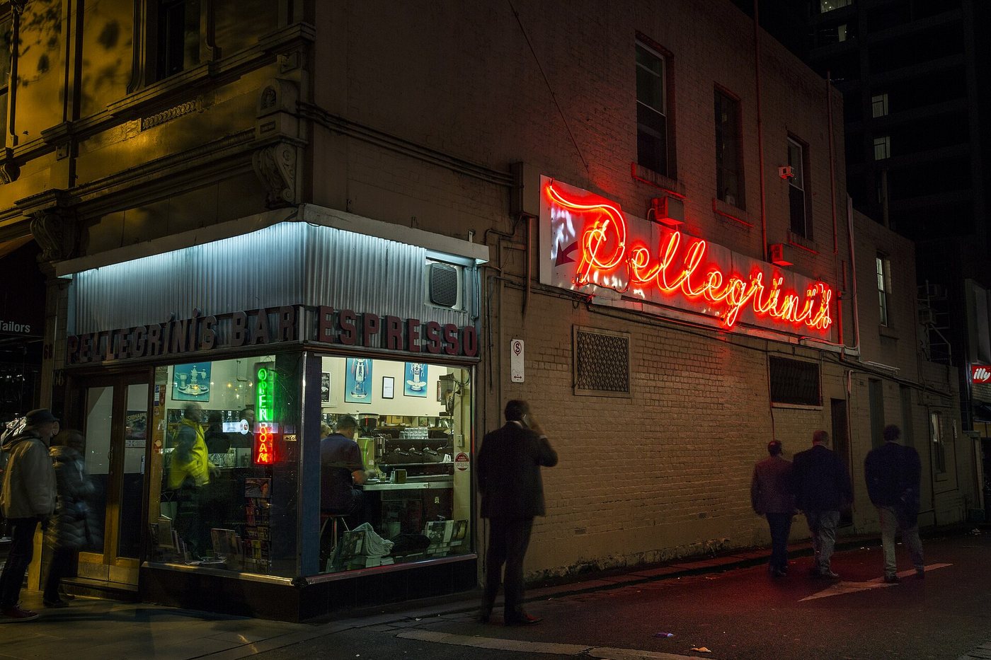 Melbourne Bourke Street'te gece çekilmiş Pellegrini's Espresso Bar; kırmızı neon tabela, cam vitrinin ardında tezgâh ve kaldırımda yürüyen insanlar