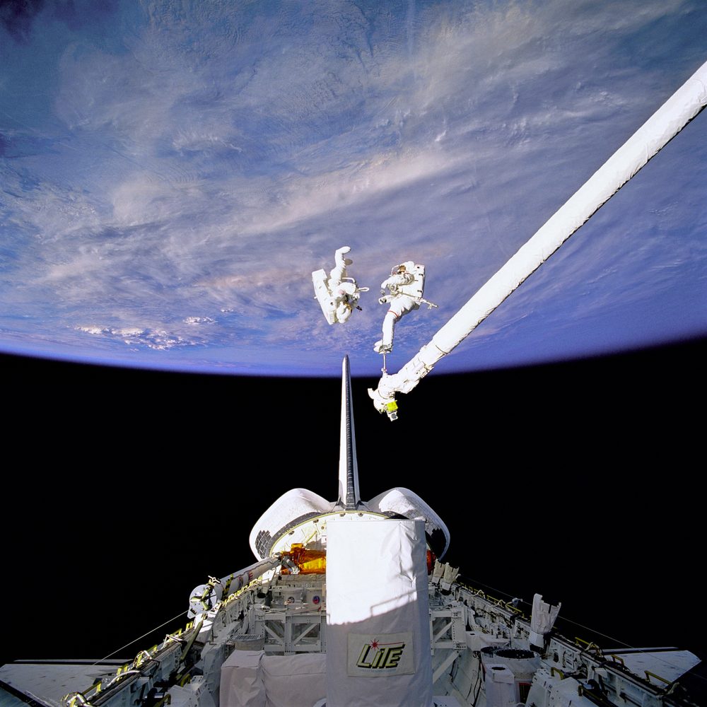 Mekiğin yük bölmesi ve robot kolunun üstünde, Dünya'nın önünde süzülen iki astronot SAFER çantasını deniyor