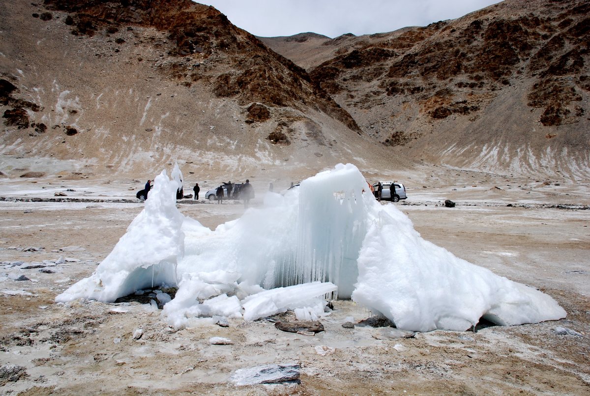 Ladakh'taki Puga vadisinde, kahverengi dağların önünde, açık renkli mineral kabuklarla kaplı düzlükte donmuş bir sıcak su kaynağının çevresinde biriken buz kütlesi