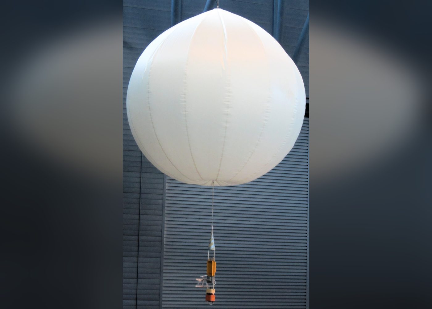 Tavana asılı beyaz, küre biçimli Vega balonunun kopyası ve altındaki ince ipe bağlı küçük turuncu ölçüm gondolu