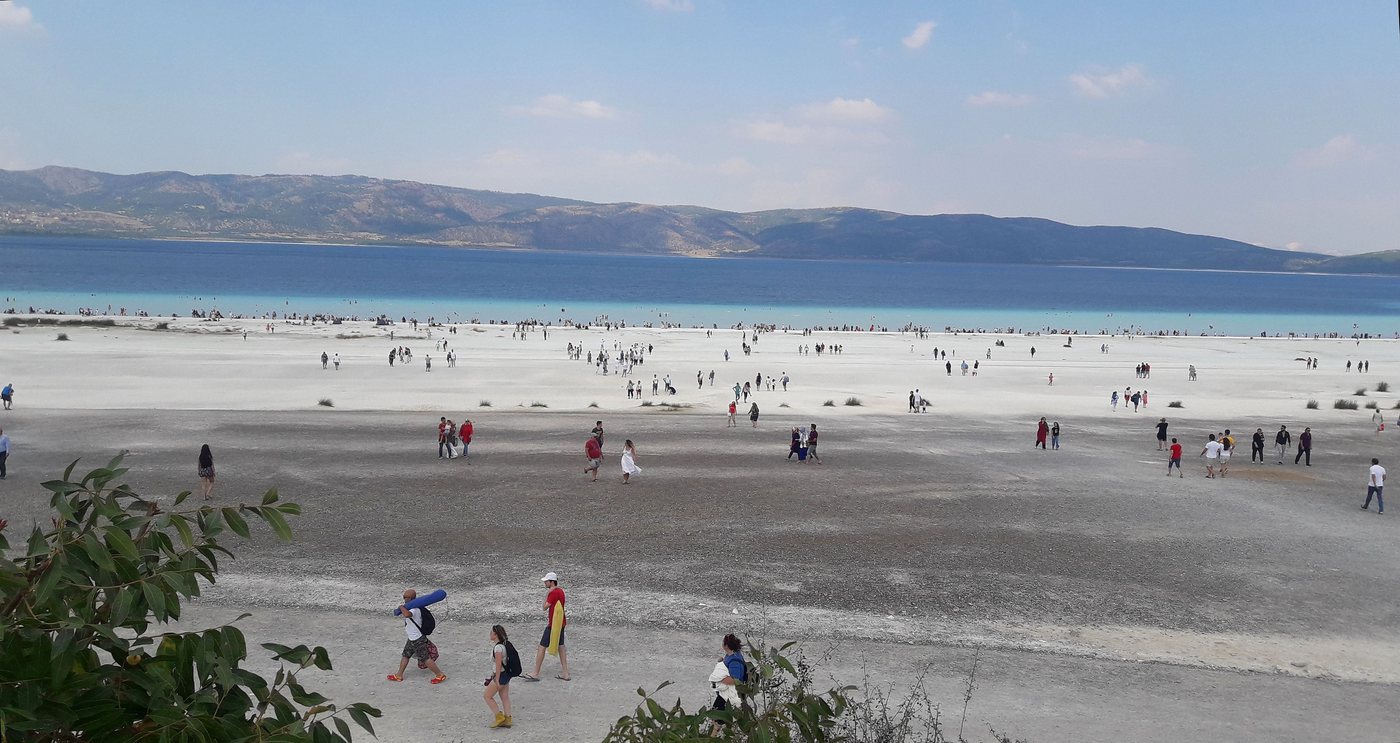 Burdur'daki Salda Gölü: turkuaz su, önünde geniş beyaz kumsal ve kumsalda yürüyen insanlar, arkada tepeler